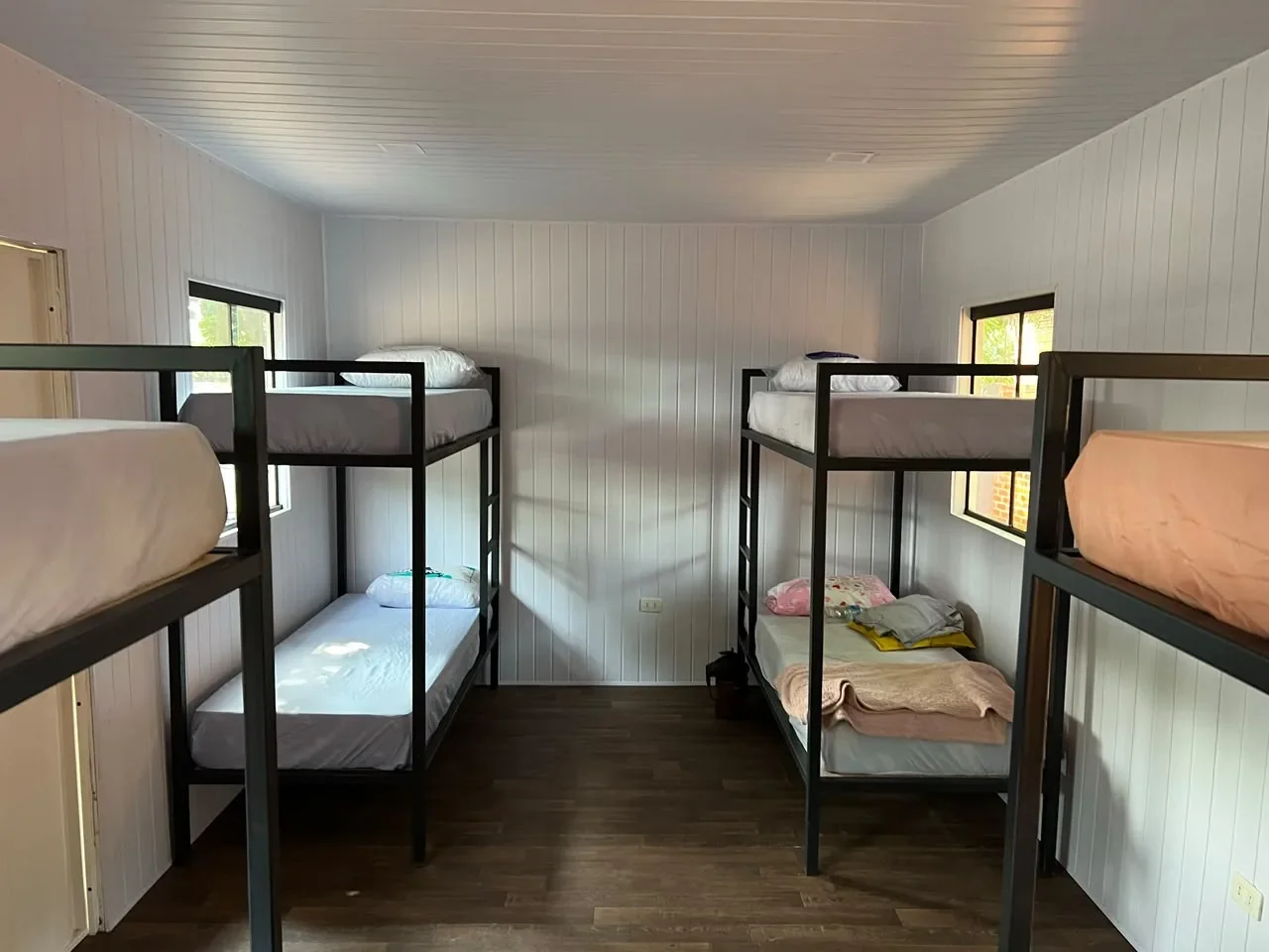 Dormitorio en contenedor con cuatro literas de hierro negro, paredes de machimbre blanco y piso de madera, uso campamento.