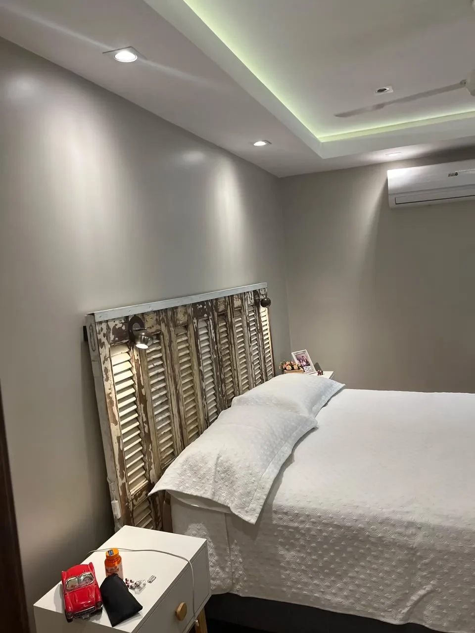 Dormitorio principal de casa de contenedor con cabecera de persianas recicladas, cielorraso cove LED y mesa de luz, estilo vintage.