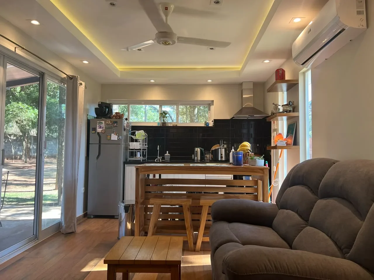 Living-cocina de casa de contenedor habitada con piso de madera, desayunador de madera, salpicadero subway negro, cielorraso con cove LED y puerta corrediza al jardin.