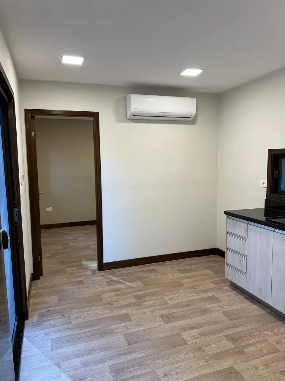 Ambiente de casa de contenedor nueva con piso laminado, puerta de madera oscura y kitchenette de granito negro, listo para entrega.