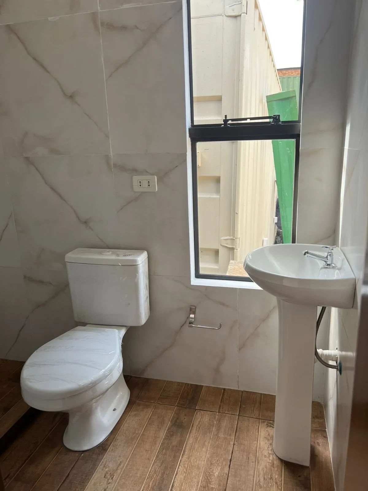 Bano de casa de contenedor nueva con porcelanato marmolado, inodoro y bacha con pedestal, listo para entrega.