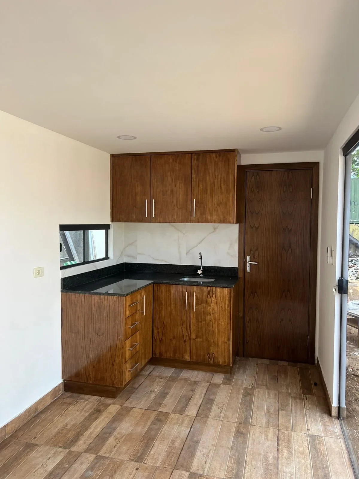 Cocina nueva de casa de contenedor con muebles de madera, mesada de granito negro, salpicadero de marmol blanco y puerta de madera, lista para entrega.