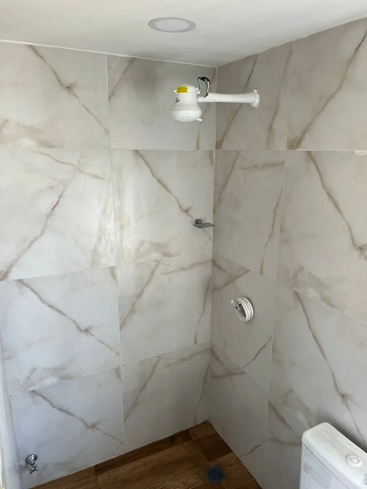 Ducha de casa de contenedor nueva con porcelanato marmolado blanco y calefon electrico, piso simil madera.