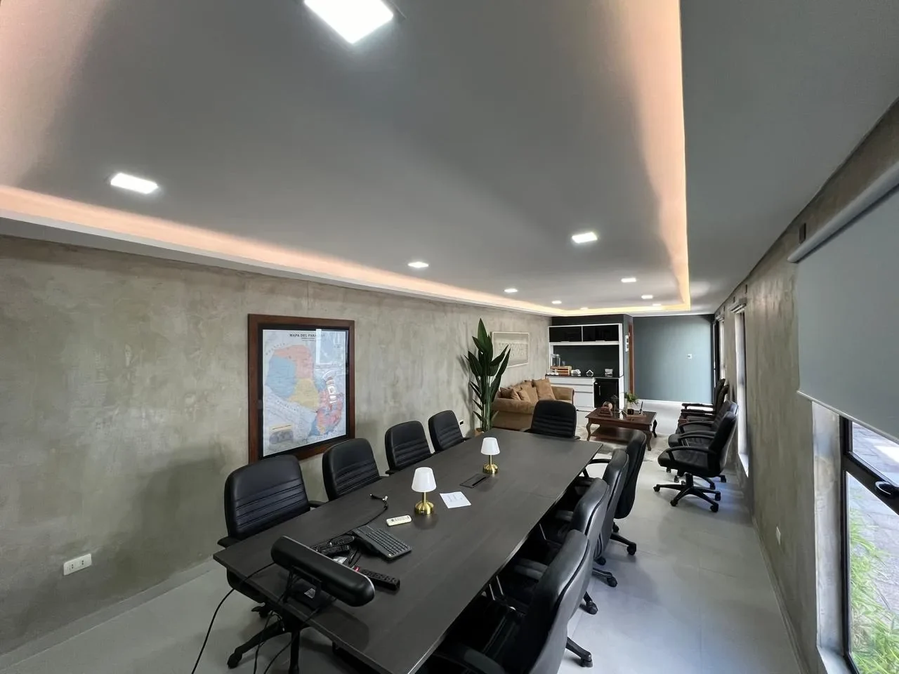 Vista amplia de la oficina ejecutiva premium en contenedor con mesa de directorio, sofa de terciopelo, mapa del Paraguay y microcemento.