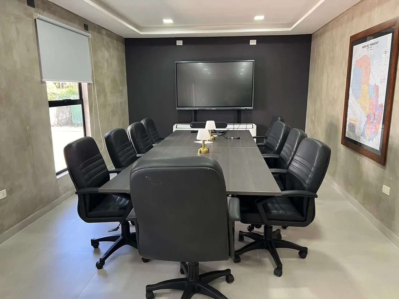 Sala de directorio en contenedor con mesa de reuniones, sillas de cuero negro, pantalla, microcemento y mapa del Paraguay.