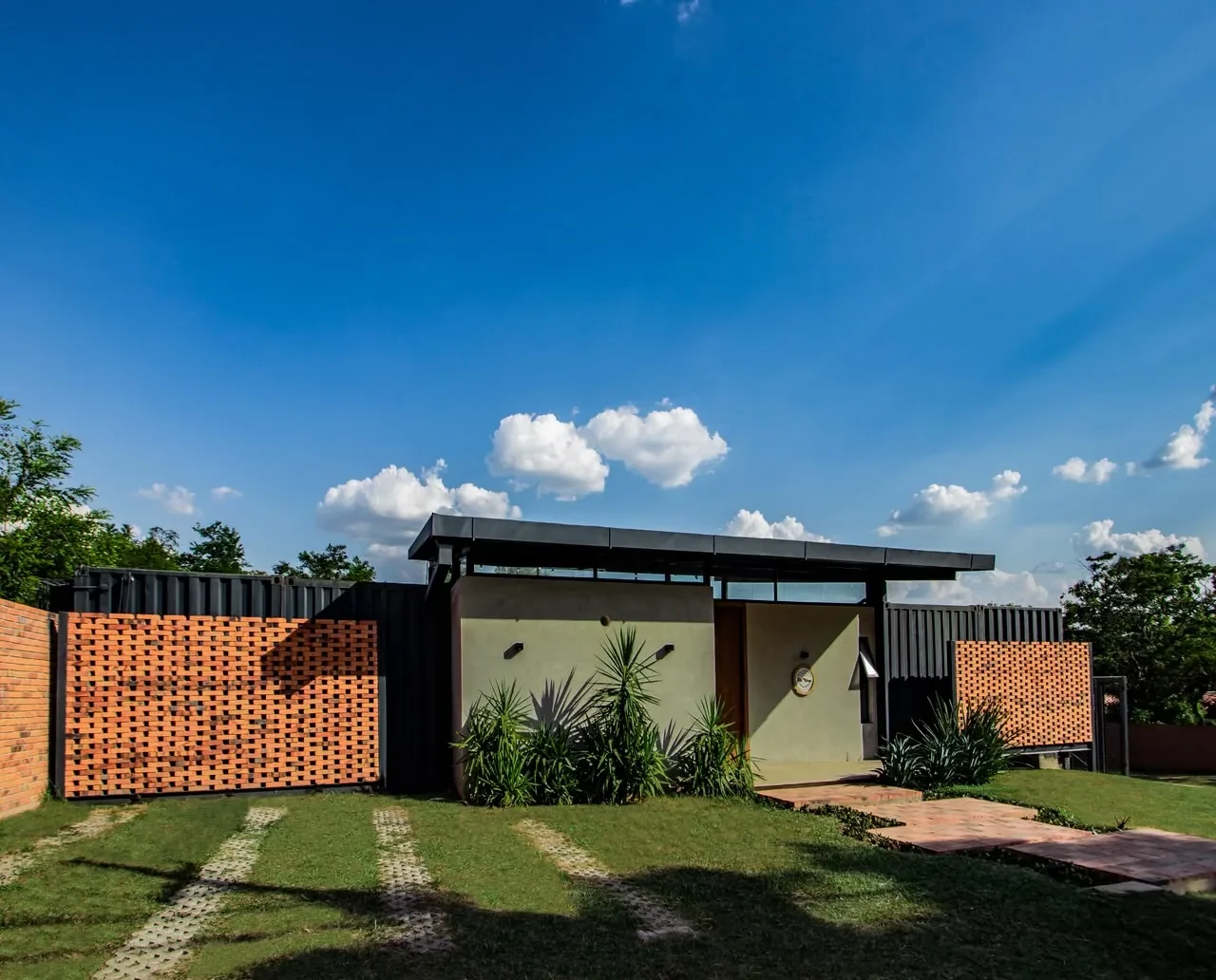Casa de contenedor oscuro detras de una celosia de ladrillo rojo calado, con techo plano y jardin, arquitectura contemporanea.